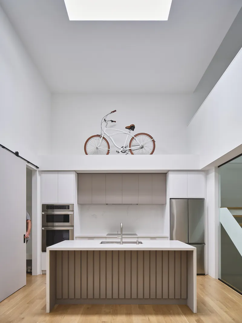 Kitchen island with fluted wood base beneath a skylight and bicycle mounted on the mezzanine ledge