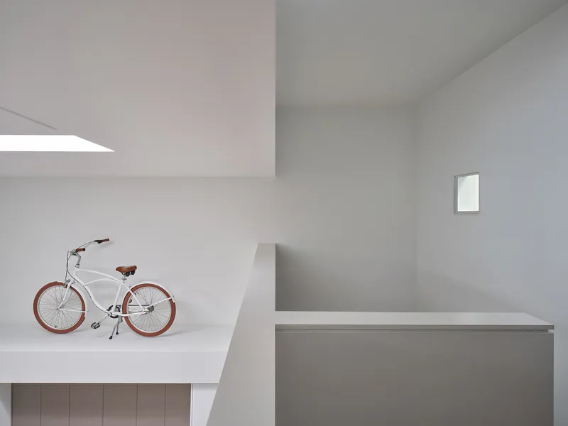 Mezzanine landing with bicycle beside a recessed skylight and small square window in the wall