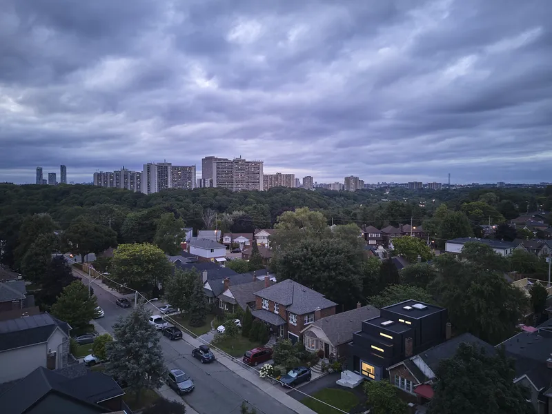 Aerial view of the black gabled house among low-rise homes under a cloudy evening sky