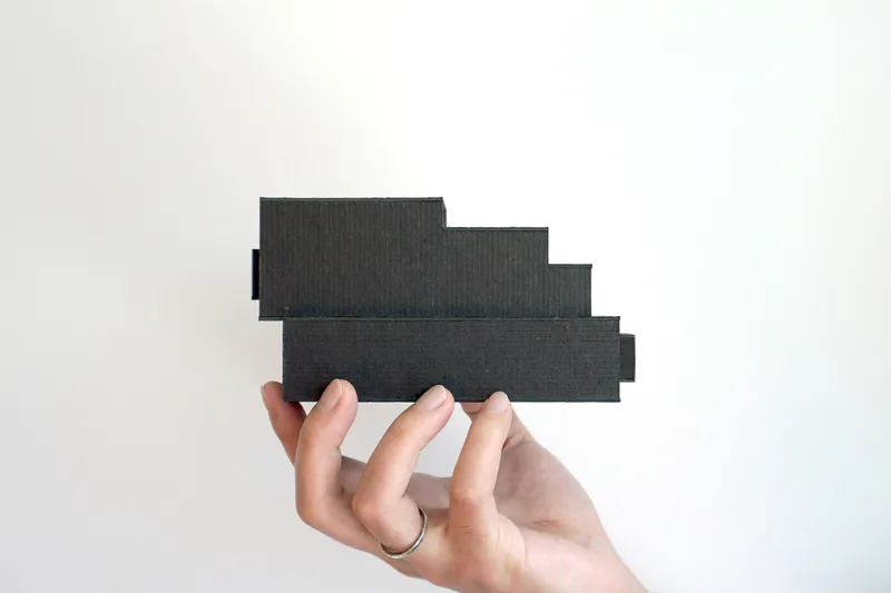Hand holding a black cardboard model of the stepped facade profile against a white background