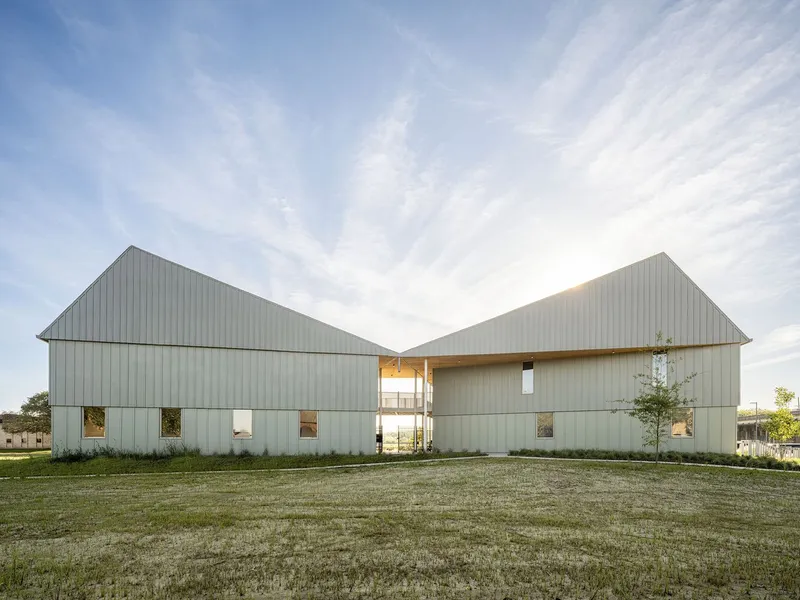 Two gabled volumes clad in vertical metal panels across an open lawn at dusk