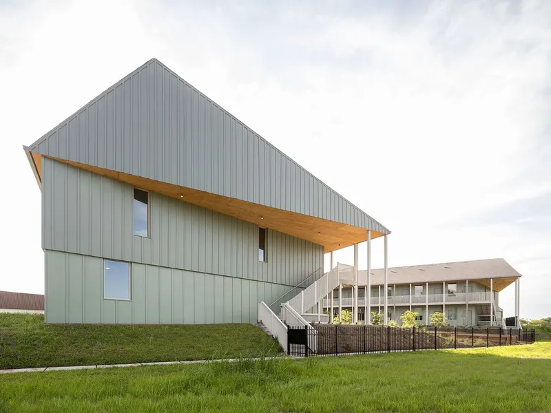 Side view of the metal-clad gabled form with timber canopy and exterior stair under overcast sky