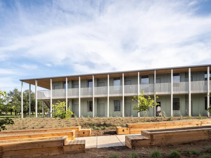 Two-story colonnade with timber soffit overlooking raised timber garden beds and young trees