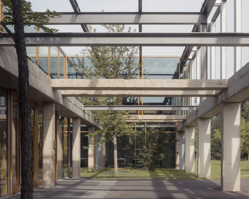 Covered outdoor passage with concrete beams and steel trusses framing views of surrounding trees