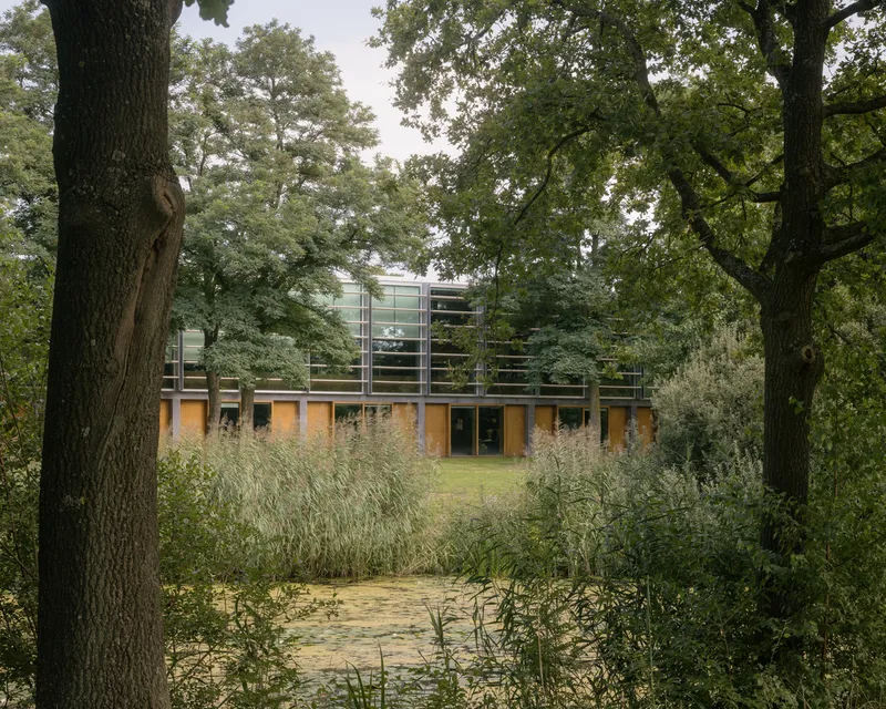 Building entrance viewed through tall grasses and mature trees in a woodland setting