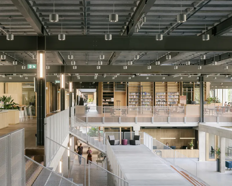 Interior view of multi-level atrium with exposed steel beams, pendant lights and glass-railed mezzanines