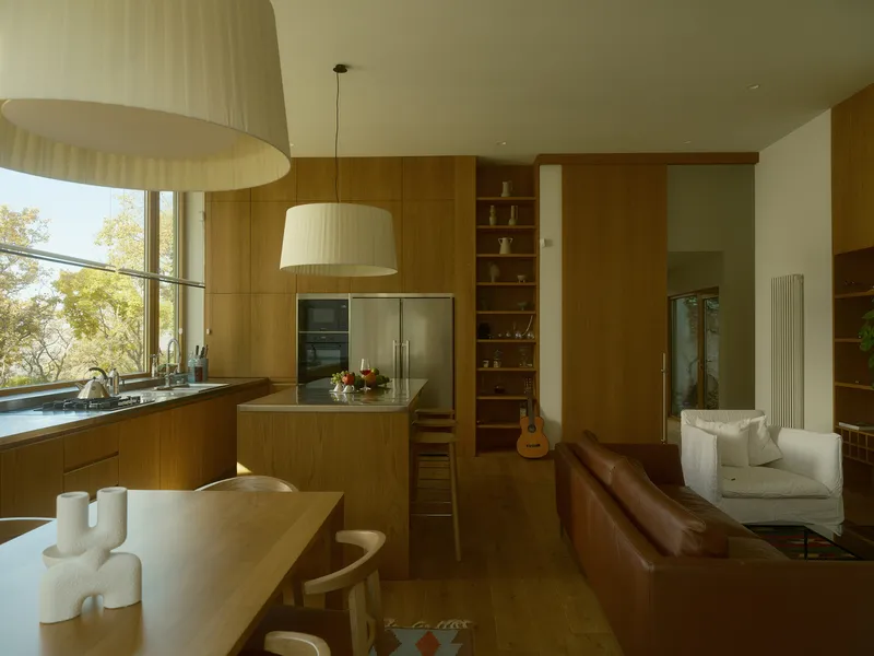 Open kitchen with wood cabinetry and pendant lights looking toward leather sofa and daybed