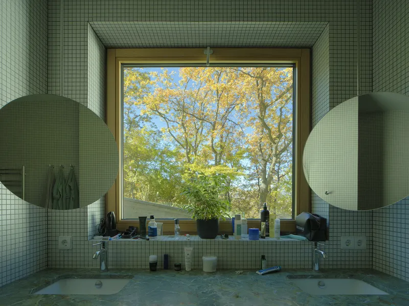 Bathroom vanity with green mosaic tile and large window framing autumn foliage