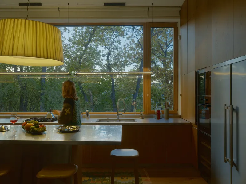 Kitchen island at dusk with figure and full-height glazing overlooking trees