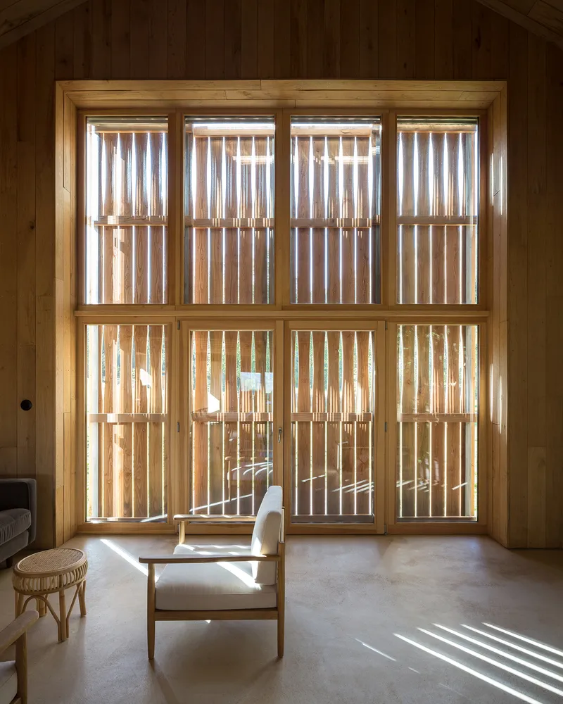 Gridded timber window wall with vertical slat screen outside filtering daylight into the seating area
