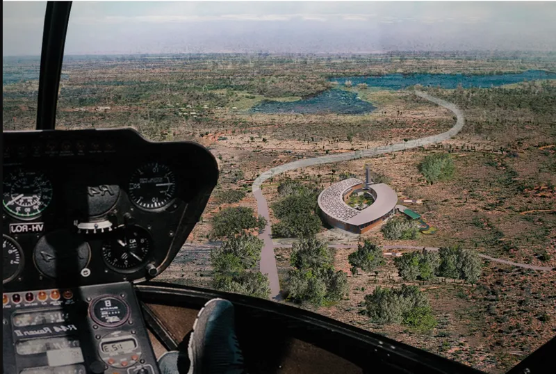 Aerial view from helicopter cockpit showing the circular building set among winding paths and sparse trees in an arid landscape