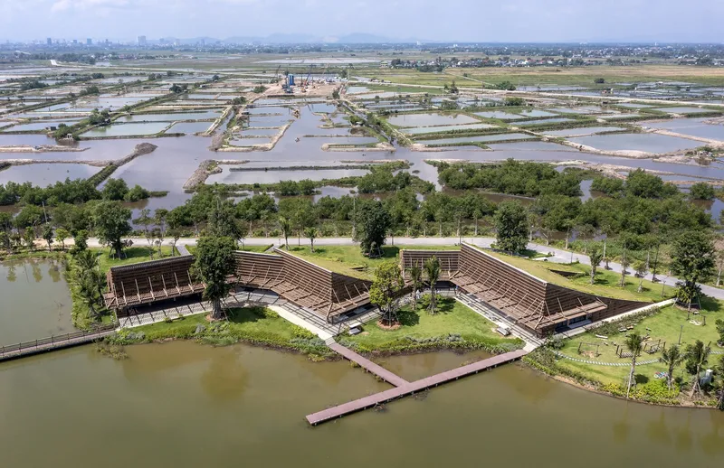 Aerial view of three clustered volumes with planted roofs on a peninsula surrounded by agricultural ponds
