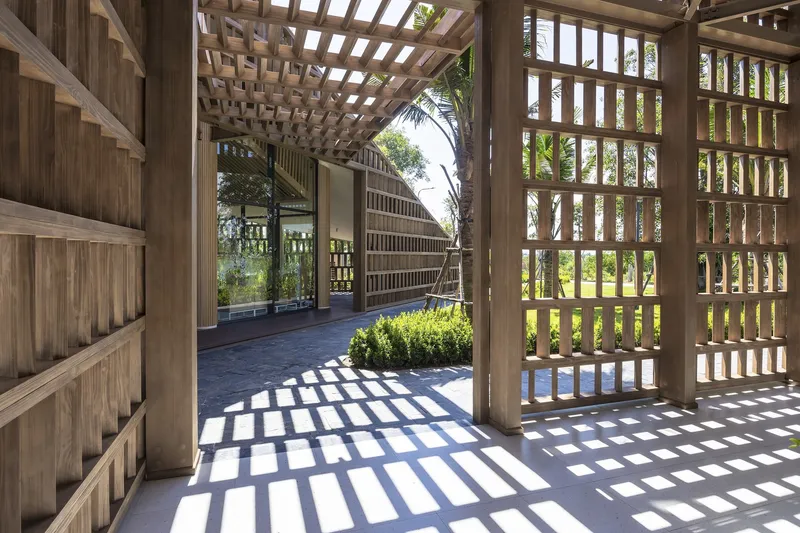 Covered walkway with timber columns and lattice screens casting geometric shadows on the floor