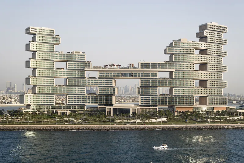 Waterfront view of the stacked horizontal tower volumes with a small boat passing in the foreground