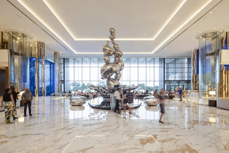 Hotel lobby with polished marble flooring and a metallic sculpture beneath a coffered cove-lit ceiling