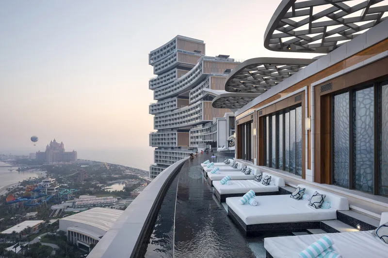 Rooftop pool terrace with white daybeds overlooking the offset tower volumes and coastline at sunset