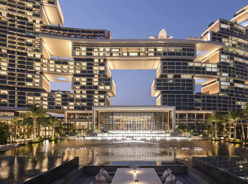 Evening view of the entrance plaza with reflecting pool and illuminated sky bridge between tower volumes