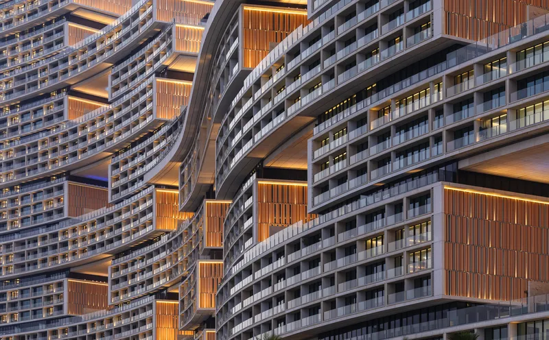 Close view of the undulating facade with horizontal balcony bands and backlit timber louvers at dusk