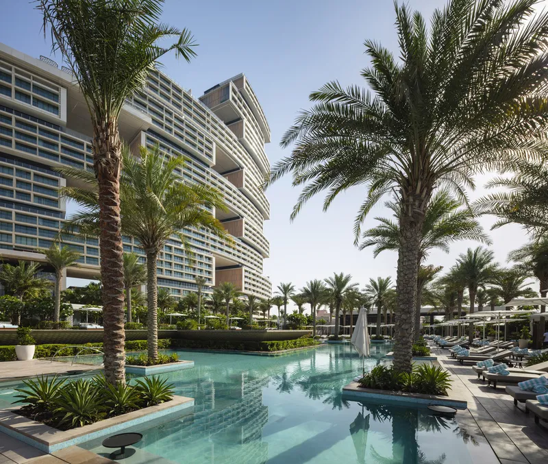 Pool deck with palm trees and tiered facade with horizontal louvered screens under bright sky