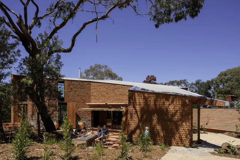 Courtyard view of the patterned brick facade with planted saplings and overhead tree branches framing the scene