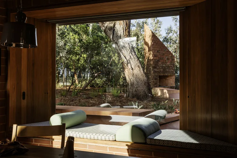 Interior window seat framing a view of the courtyard with a leaning tree trunk and brick volume beyond