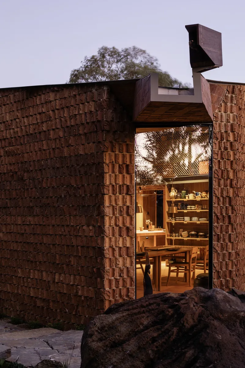 Entrance through textured brick walls opening to illuminated dining area at dusk