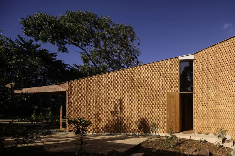 Facade with basketweave brick pattern and a tall narrow doorway under the evening sky