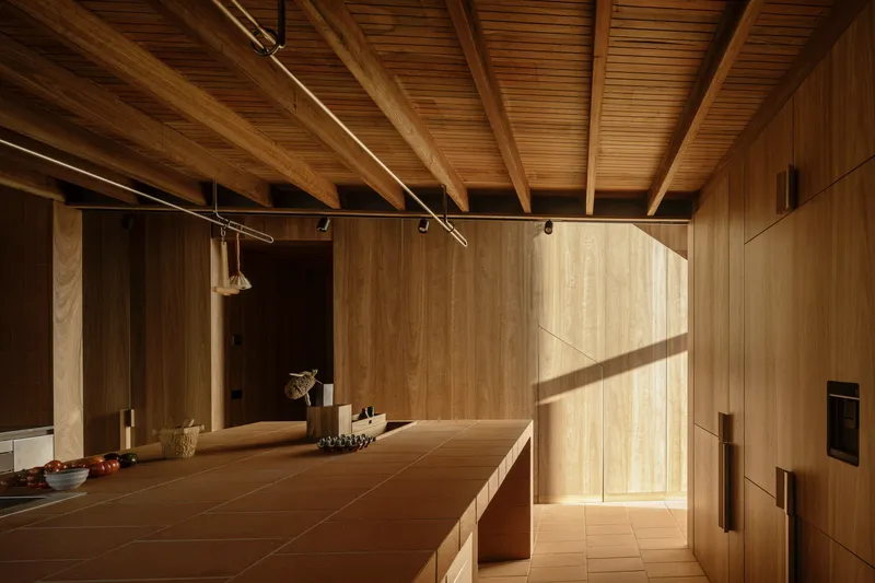 Kitchen island with timber cabinetry under exposed beam ceiling in afternoon sunlight