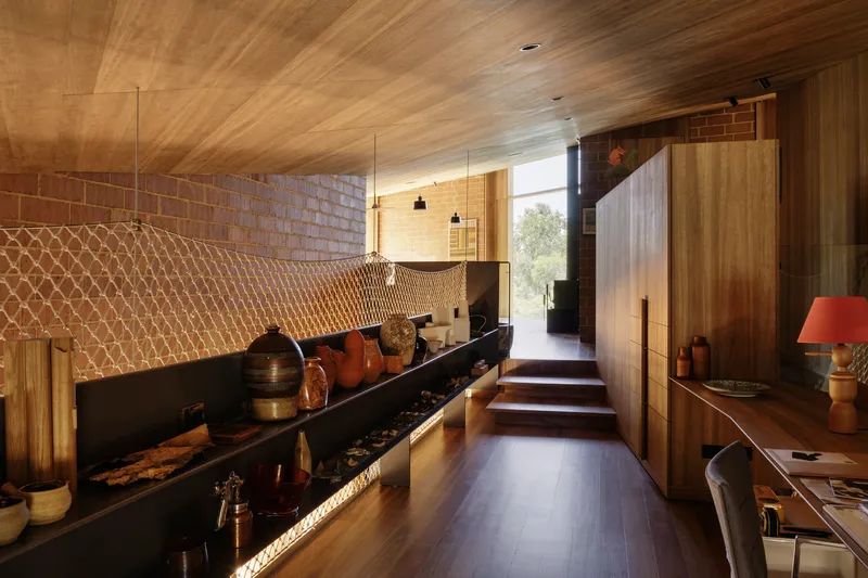 Corridor with mesh wall panel and timber surfaces leading toward glazed entry
