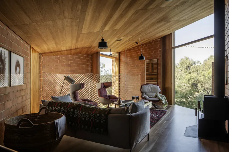 Living room with timber ceiling, terracotta brick walls, rope net partition and wood stove near glazed corner