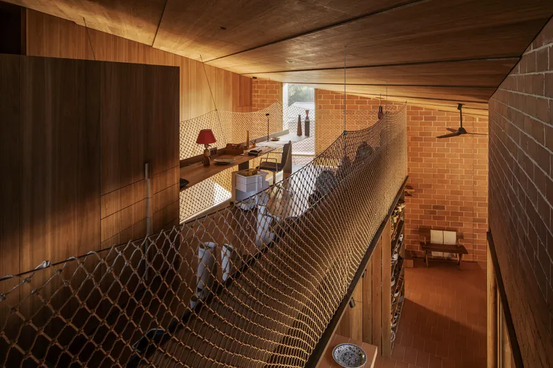 Rope mesh netting suspended between timber-clad walls and terracotta brick volumes across two levels