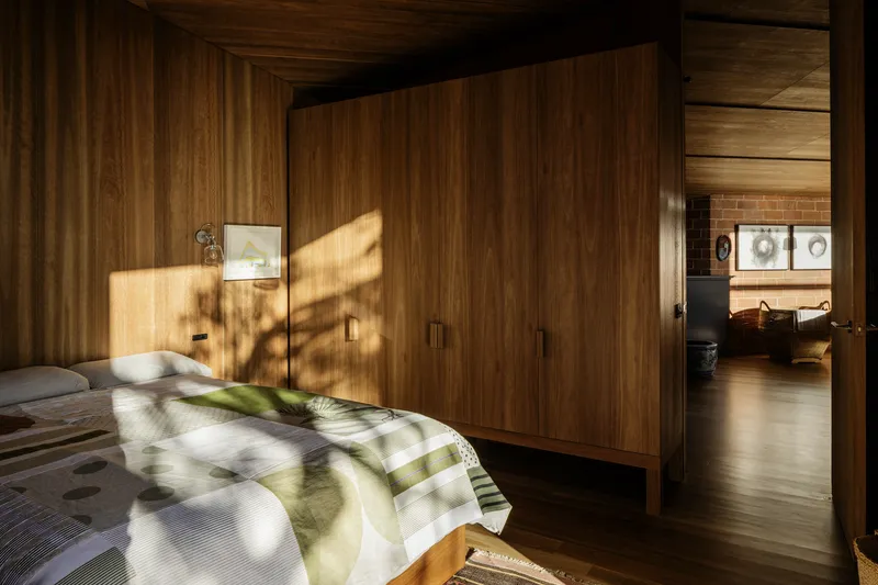 Bedroom with timber paneled walls and built-in wardrobe in morning light casting tree shadows