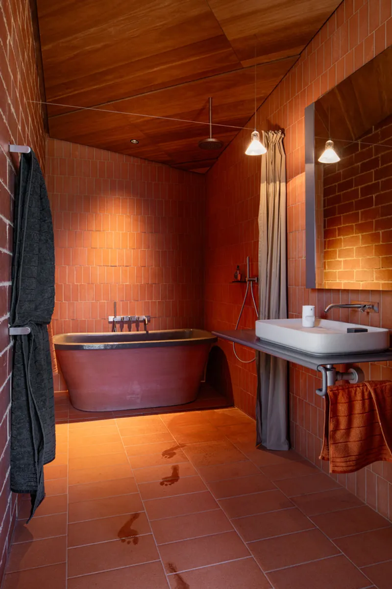 Bathroom with terracotta brick walls, copper freestanding tub, timber ceiling and pendant lights