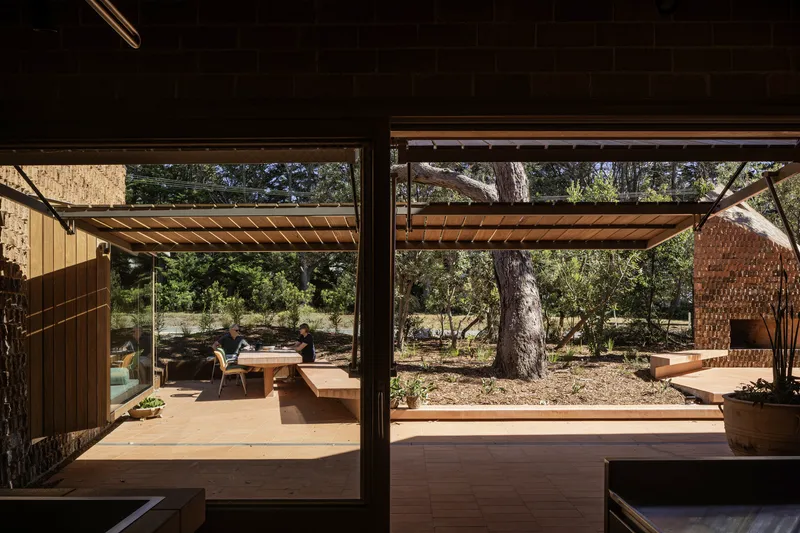 View through glazed walls to covered terrace with timber slat roof and native trees beyond