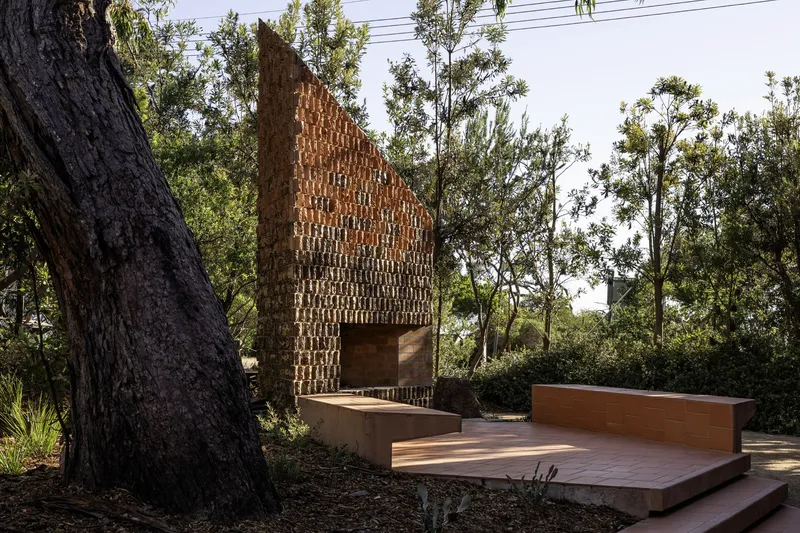Gabled brick facade with patterned masonry and timber deck terrace surrounded by eucalyptus trees