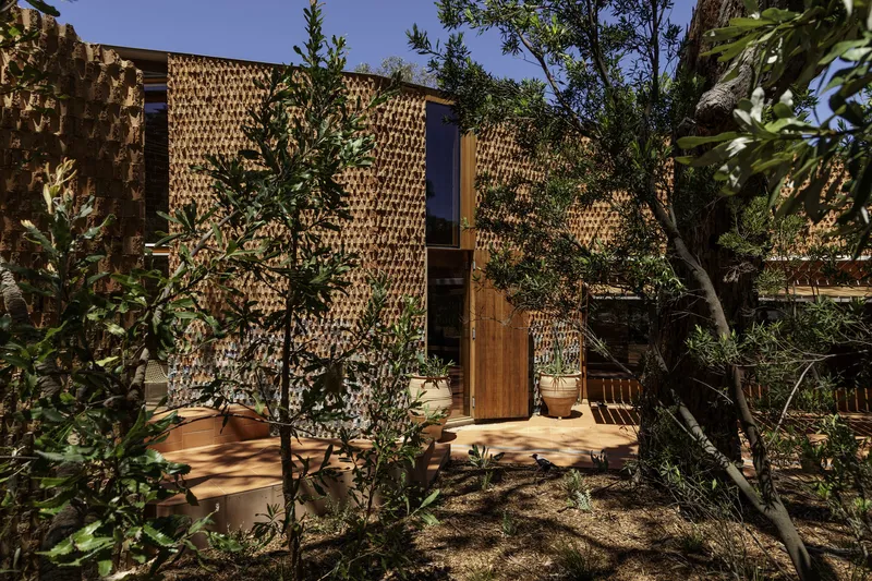 Brick volumes with timber doorway nestled among native trees and planted garden beds