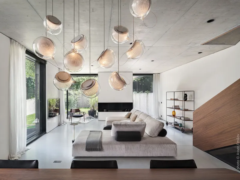 Living room with suspended glass sphere pendants, exposed concrete ceiling, and the timber stair rising at the right edge