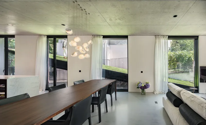Dining space with floor-to-ceiling windows framing lawn and pendant light above walnut table