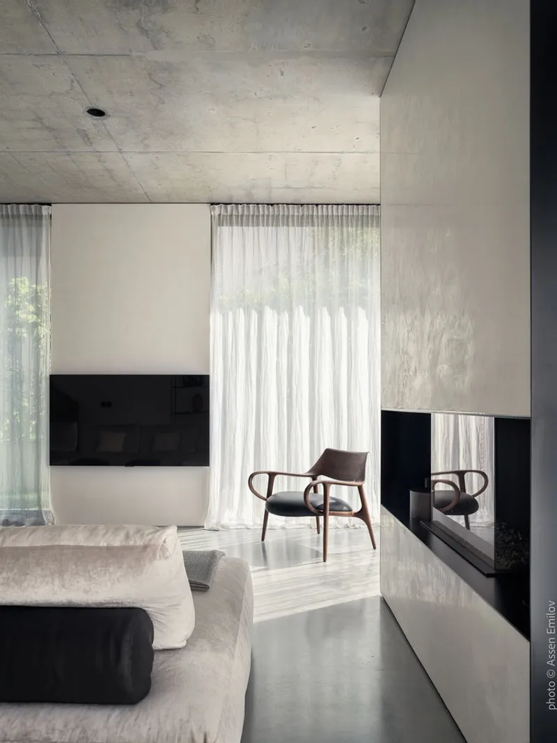 Living room with exposed concrete ceiling, black fireplace surround and sheer curtains filtering daylight