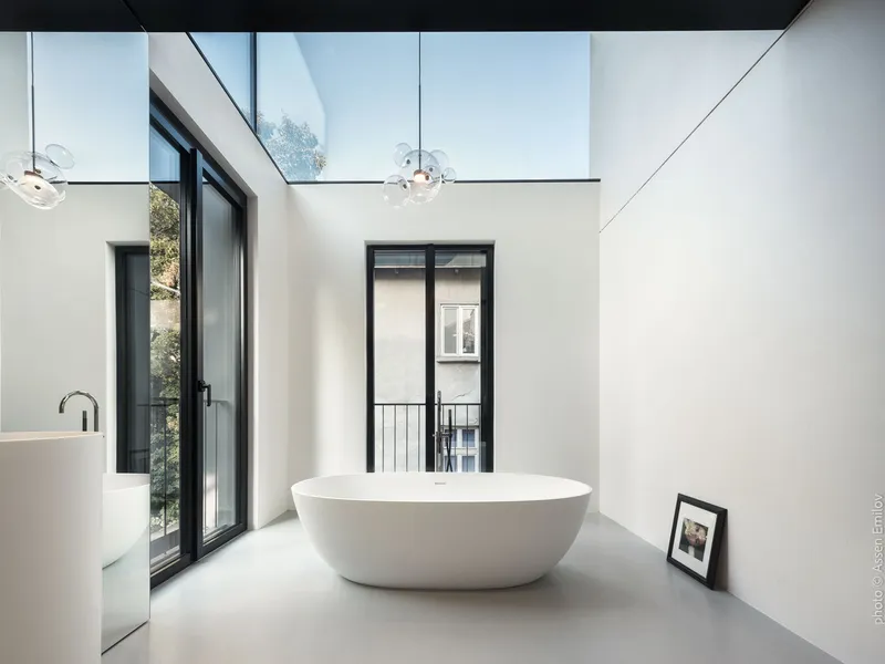 Freestanding white bathtub beneath a skylight with glass pendant lights and black-framed doors