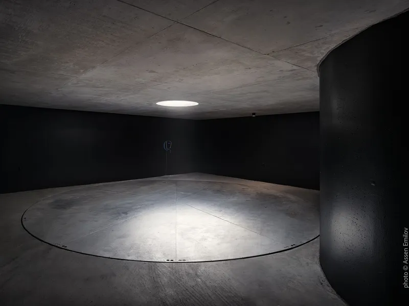 Circular garage turntable in a basement space with black walls and overhead skylight