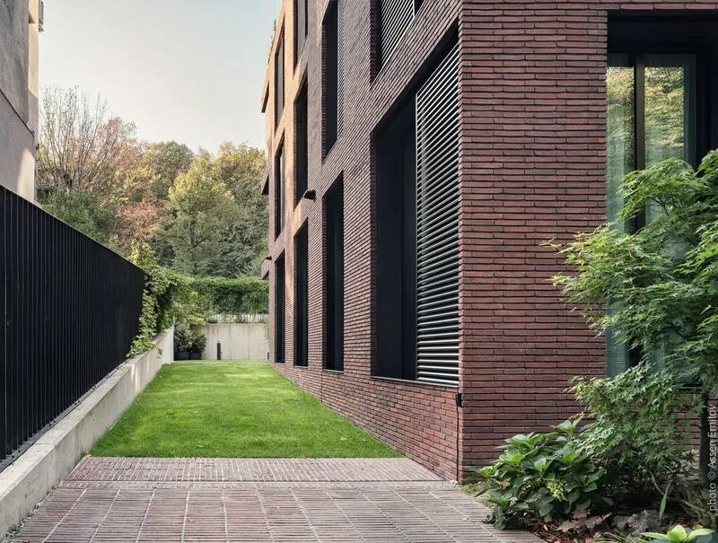 Narrow courtyard with grass lawn between brick facade and corrugated metal fence in afternoon light