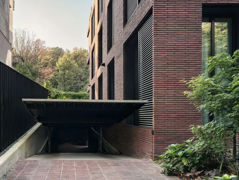 Cantilevered metal canopy over parking entry ramp flanked by brick walls and green lawn