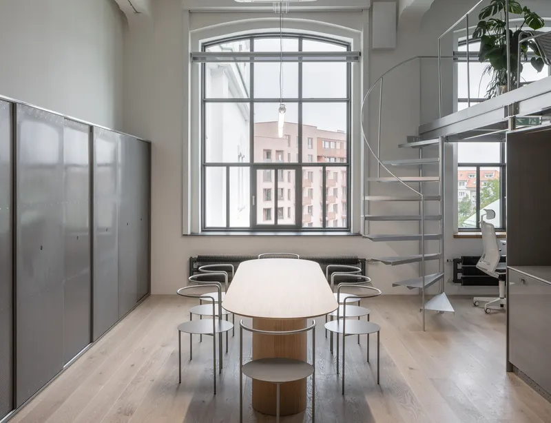 Double-height dining area with arched window overlooking neighboring buildings and a curved metal staircase