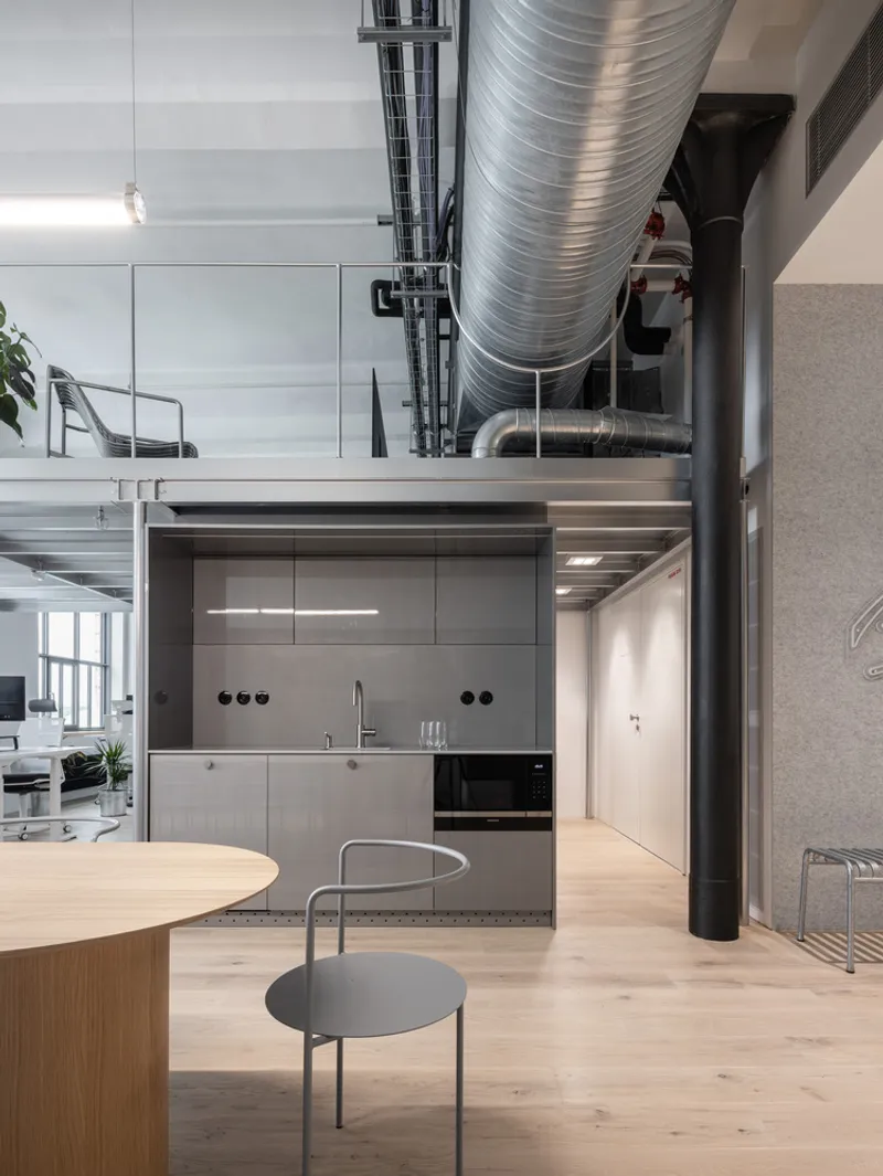 Compact kitchenette with gray cabinetry beneath exposed spiral ductwork and a black steel column