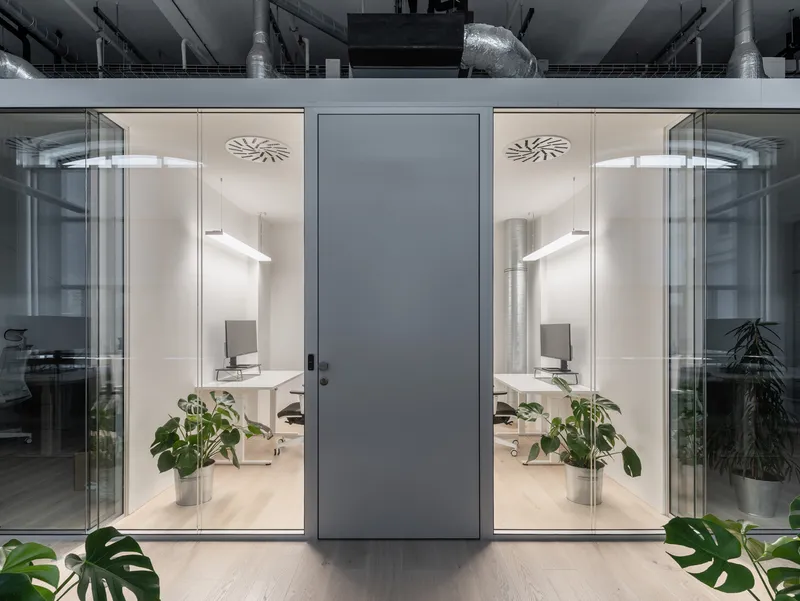 Symmetrical glass-walled offices flanking a central gray door with potted plants in the foreground