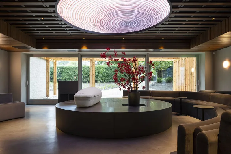 Interior lounge with circular ceiling pendant above a round table holding a red-leafed branch