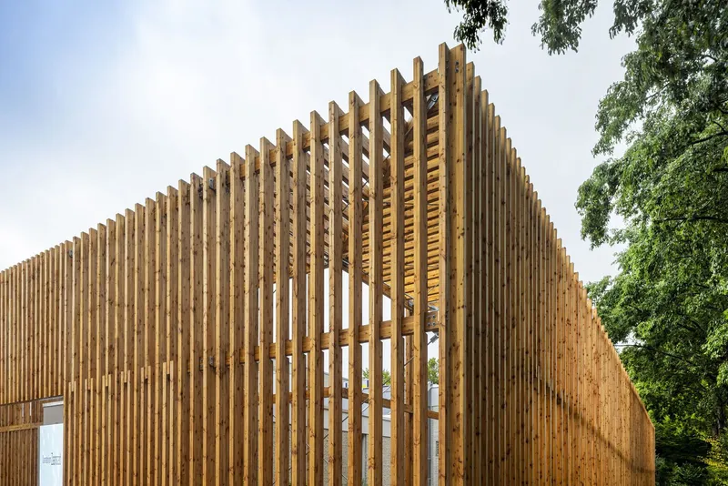 Vertical timber slat screen with angled gable profile framed by mature trees