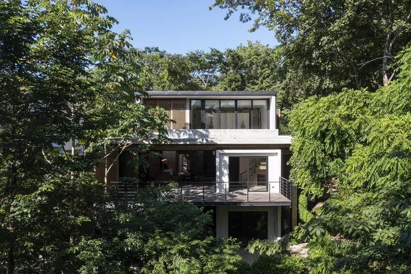 Three-level facade nestled into the wooded hillside with cantilevered upper floors and glazed openings