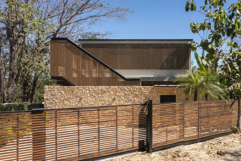 Street view showing horizontal timber fence and stone retaining wall beneath the elevated upper volume